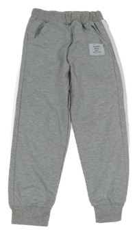 Šedé tepláky s bílými pruhy a nášivkou 